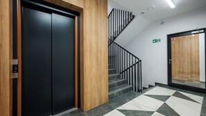A modern elevator with a digital display, a staircase with black railings, and a patterned floor. - Malinova Leaf Apartment (Warszawa)