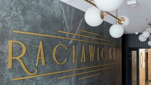 A modern interior with a marble wall displaying the name 'RACLAWICKE' in gold lettering, a contemporary light fixture, and a door with a circular logo. - Malinova Leaf Apartment (Warszawa)