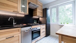 A modern kitchen with wooden cabinets, a stainless steel refrigerator, a Bosch dishwasher, and a window with a view of greenery. - Osiedle Sobieskiego Comfort Apartment (Poznań)