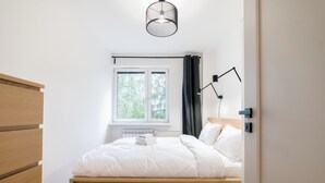 A bedroom with a wooden bed, a window, a radiator, and a bedside table. - Osiedle Sobieskiego Comfort Apartment (Poznań)