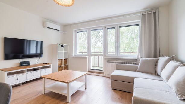 A modern living room with a flat-screen TV, a wooden coffee table, a sofa, and a window with curtains. - Osiedle Sobieskiego Comfort Apartment (Poznań)