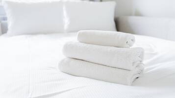 Un llit ben fet amb llençols i almoades blanques, i una tovallola blanca plegada a la part superior, amb una finestra i cortines al fons.