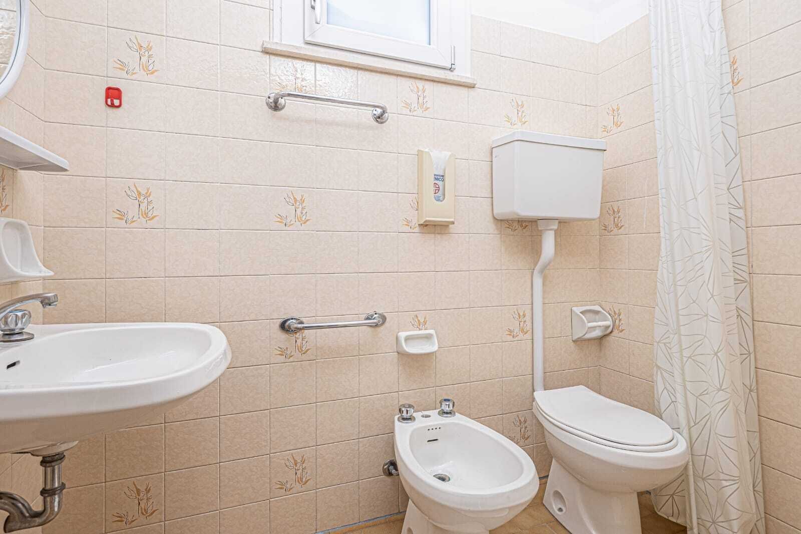A bathroom with a sink, toilet, bidet, and grab bars.