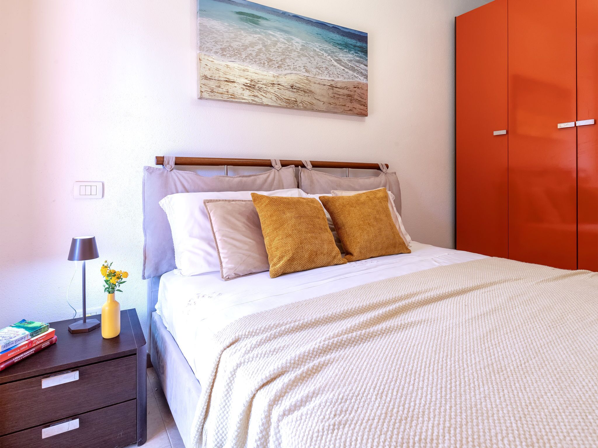A neatly arranged bedroom with a bed, bedside table, lamp, and a painting on the wall.
