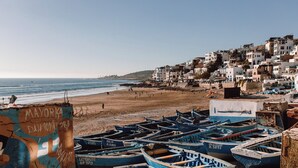 A beach with boats and buildings in the background. - Best room with WiFi in taghazout (agadir)