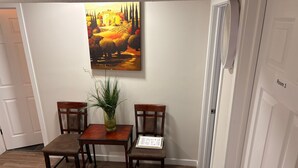 A dining area with a table and two chairs, a vase with green plants, and a painting on the wall.