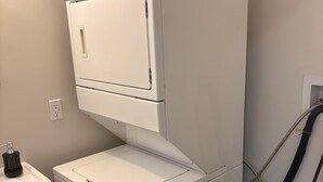 A compact laundry room with a stacked washer and dryer, a sink, and a blue recycling bin.