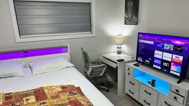 A hotel room with a bed, a desk with a computer, a TV, and a lamp.