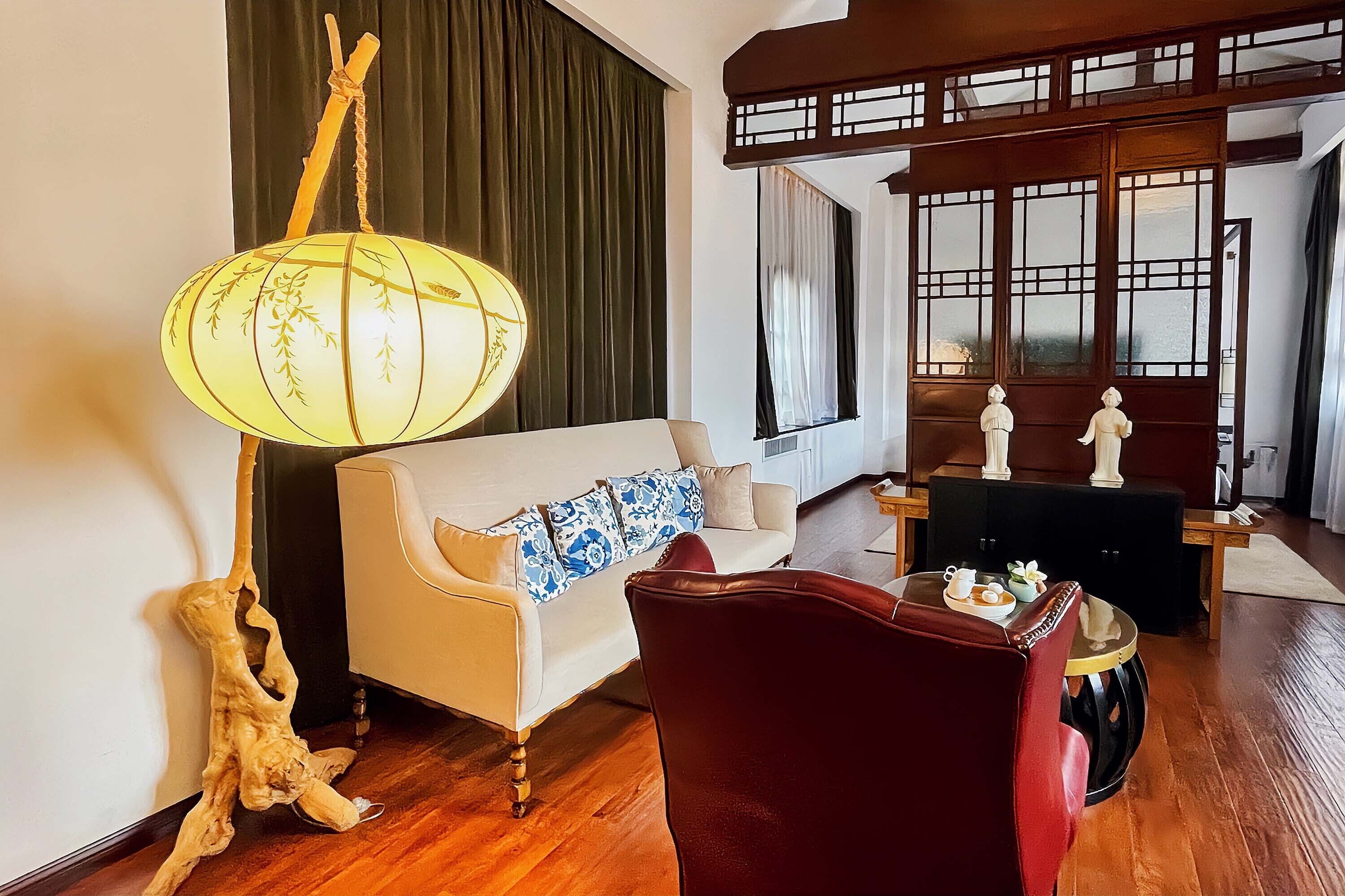 A room with a sofa, a red chair, a table with a lamp, and a decorative piece.