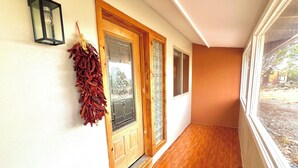 Un couloir avec un plancher en bois, un paillasson sur lequel est écrit « bonjour », et une plante séchée suspendue.
