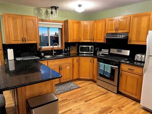 Une cuisine avec des meubles de rangement en bois, un plan de travail noir, un évier en acier inoxydable, un four à micro-ondes, une cuisinière et un réfrigérateur.