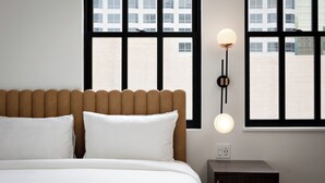 Habitación de hotel con cama, dos lámparas de noche y grandes ventanales con vista a la ciudad.