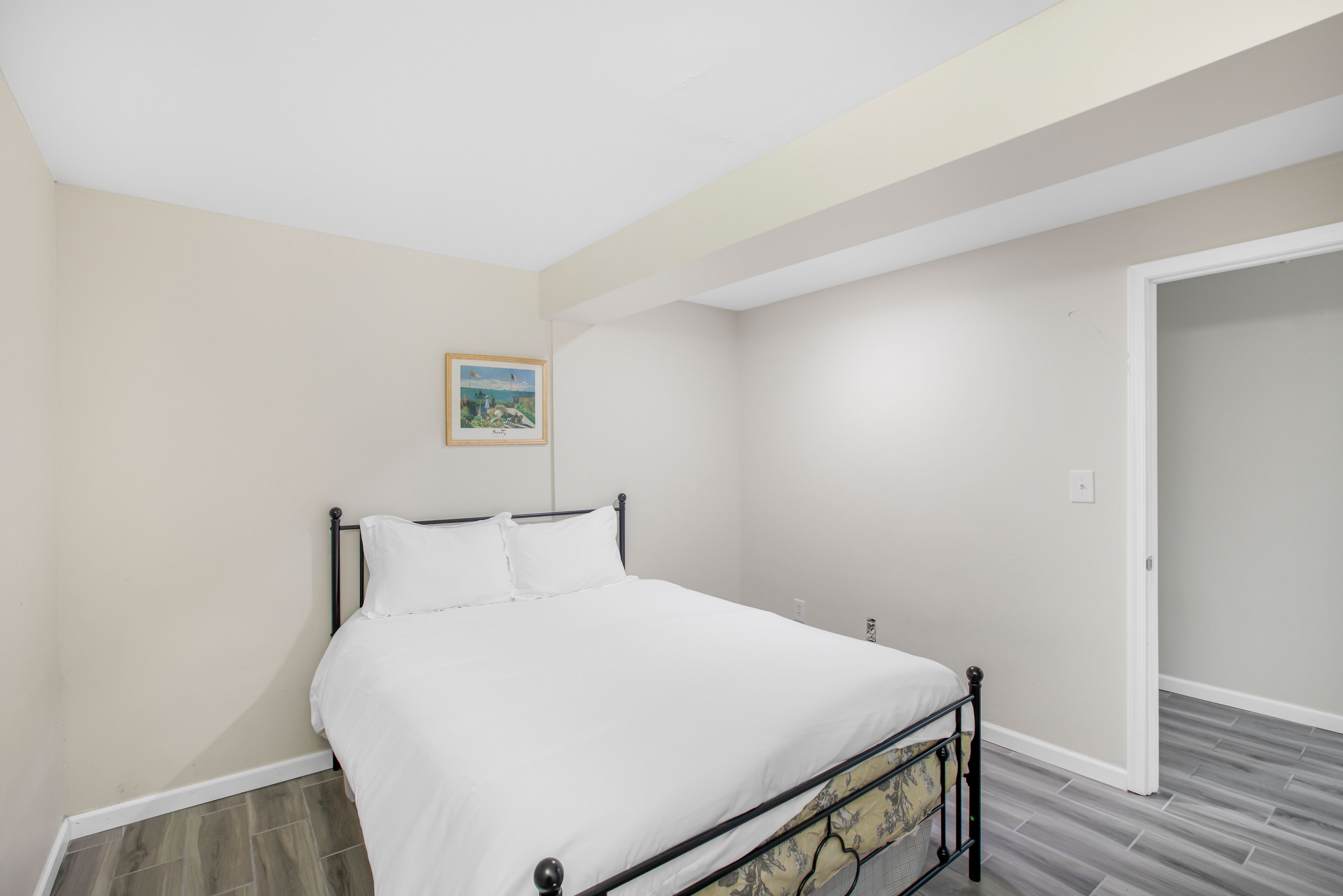 Un dormitorio con una cama, un cuadro enmarcado en la pared y una puerta que da a otra habitación.