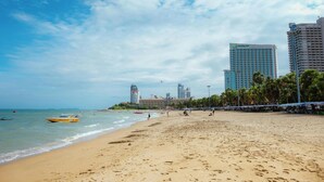 Una playa con una hilera de edificios altos al fondo, incluyendo un hotel con un letrero visible.