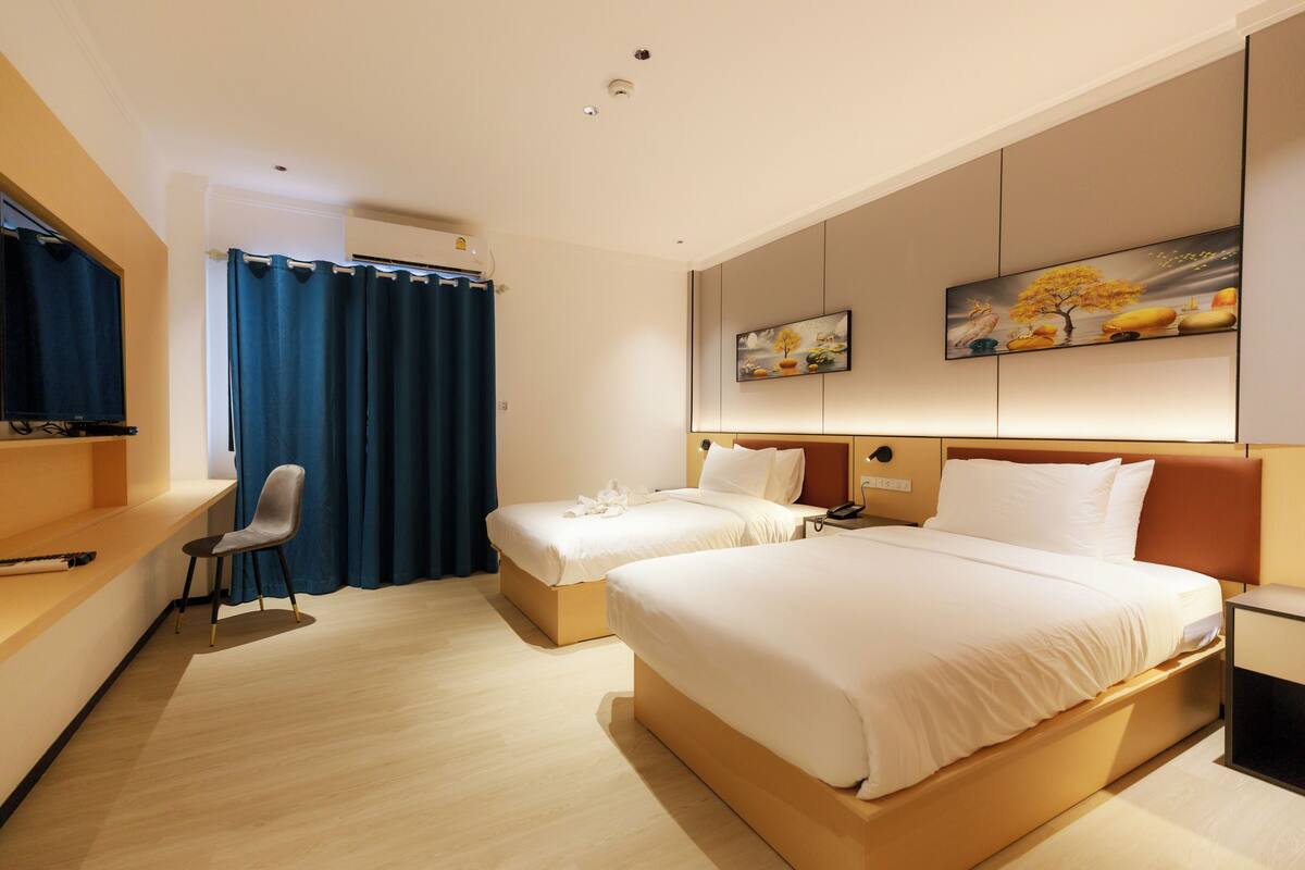 A hotel room with two beds, a desk, a chair, and a large window with curtains.