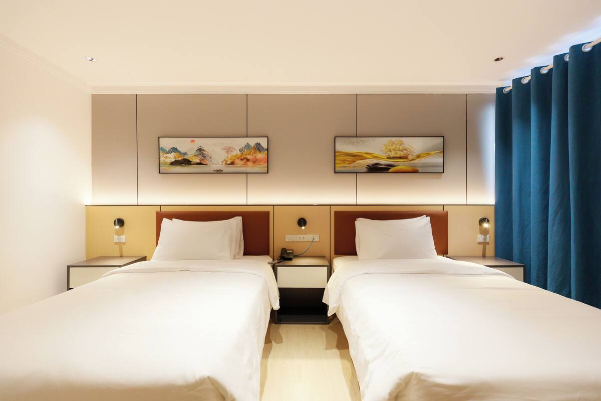 A hotel room with two beds, a nightstand with a phone, and artwork on the wall.