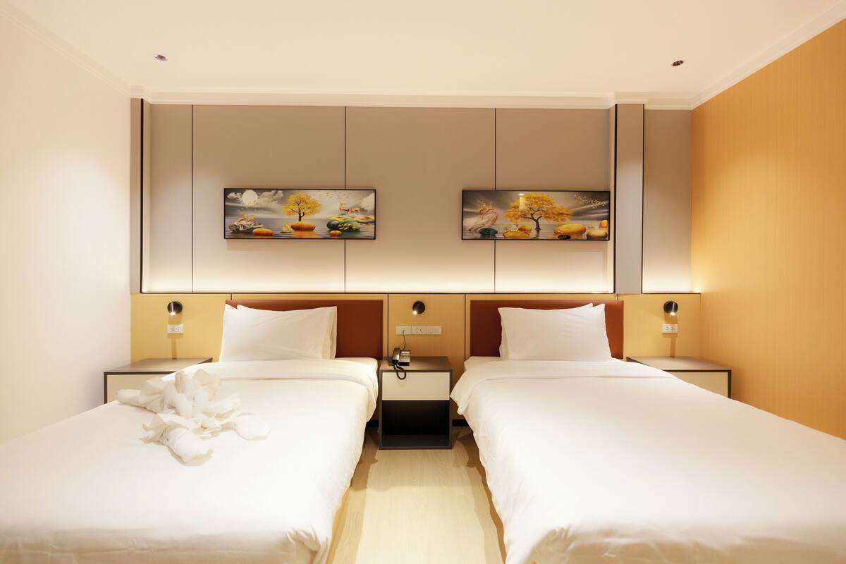 A hotel room with two beds, a nightstand with a phone, and artwork on the wall.