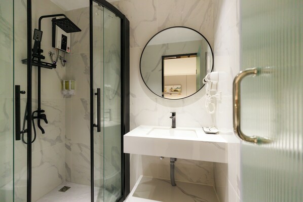 Un baño moderno con ducha de vidrio, lavamanos blanco y espejo redondo.