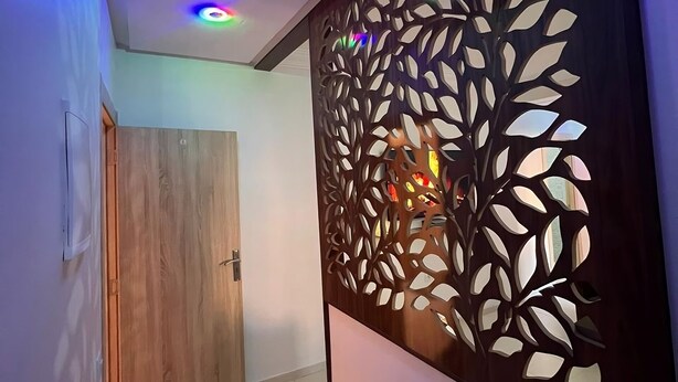 Un pasillo con puerta de madera, un panel decorativo con motivos de hojas y luces en el techo.