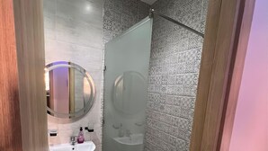 Un baño moderno con ducha envuelta en vidrio, un espejo redondo y un lavabo pedestal.