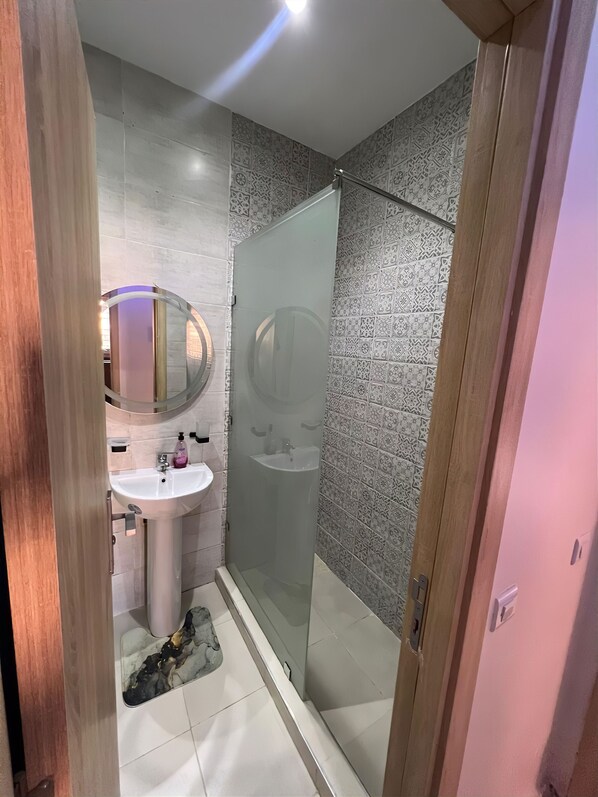 Une salle de bain moderne avec une douche à parois de verre, un miroir rond et un lavabo sur colonne.