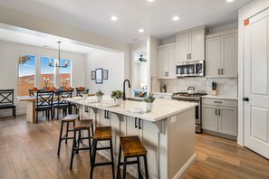 A modern kitchen with white cabinetry, a central island with stools, and a dining area with a view.