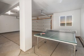 A ping pong table in a room with a garage door and a window with blinds. - Paseos Retreat: 2 Luxury Homes w/ Pool, Hot Tubs, Game Rooms, & Resort Access (Washington)