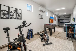 Ginásio em casa com equipamentos de exercício, mesa de futebol de mesa e obras de arte nas paredes.