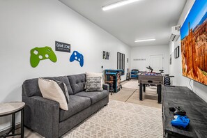 A room with a grey sofa, a foosball table, and wall decorations including game controller silhouettes and a 'GAME ZONE' sign. - Paseos Retreat: 2 Luxury Homes w/ Pool, Hot Tubs, Game Rooms, & Resort Access (Washington)
