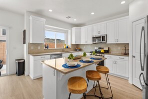 A modern kitchen with white cabinetry, a central island with stools, a microwave, and a stove.