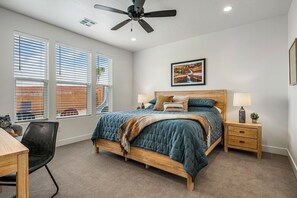 A bedroom with a bed, two bedside tables, a ceiling fan, and a window with blinds.