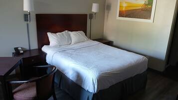 Habitación de hotel con una cama individual, un escritorio con silla, un teléfono y dos lámparas fijadas a la pared.