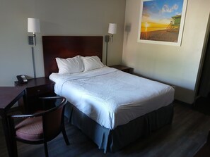 Et hotelværelse med en enkelt seng, et skrivebord med stol, en telefon og to væglamper.