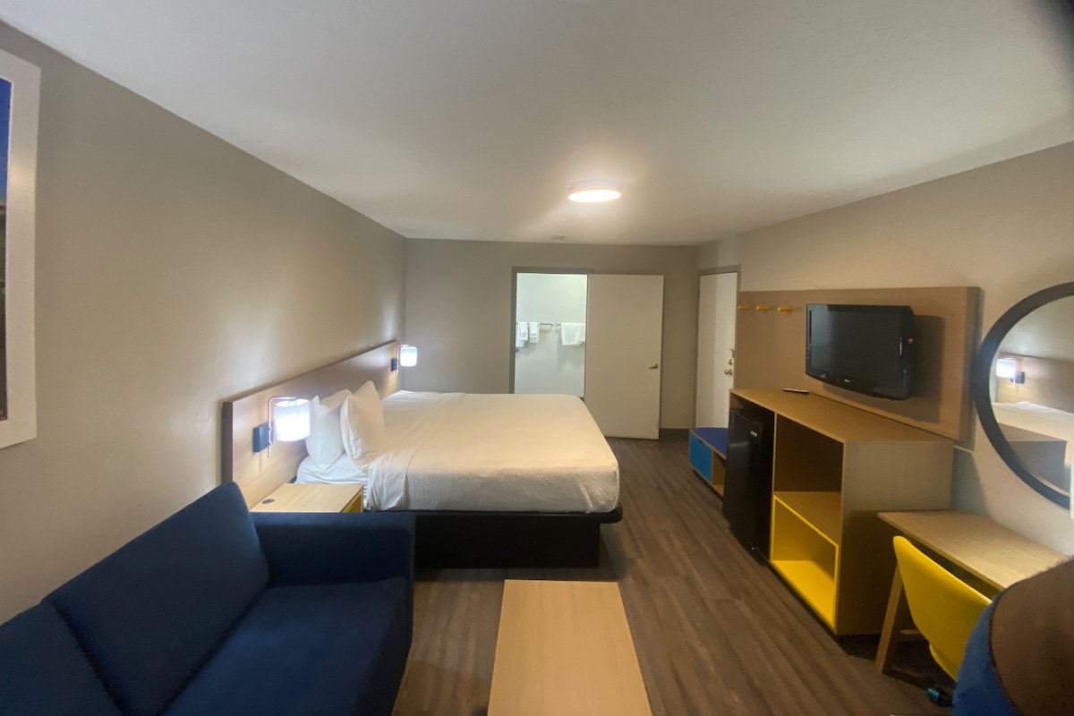 Una habitación de hotel con una cama, un sofá azul, un escritorio, un televisor y un espejo.
