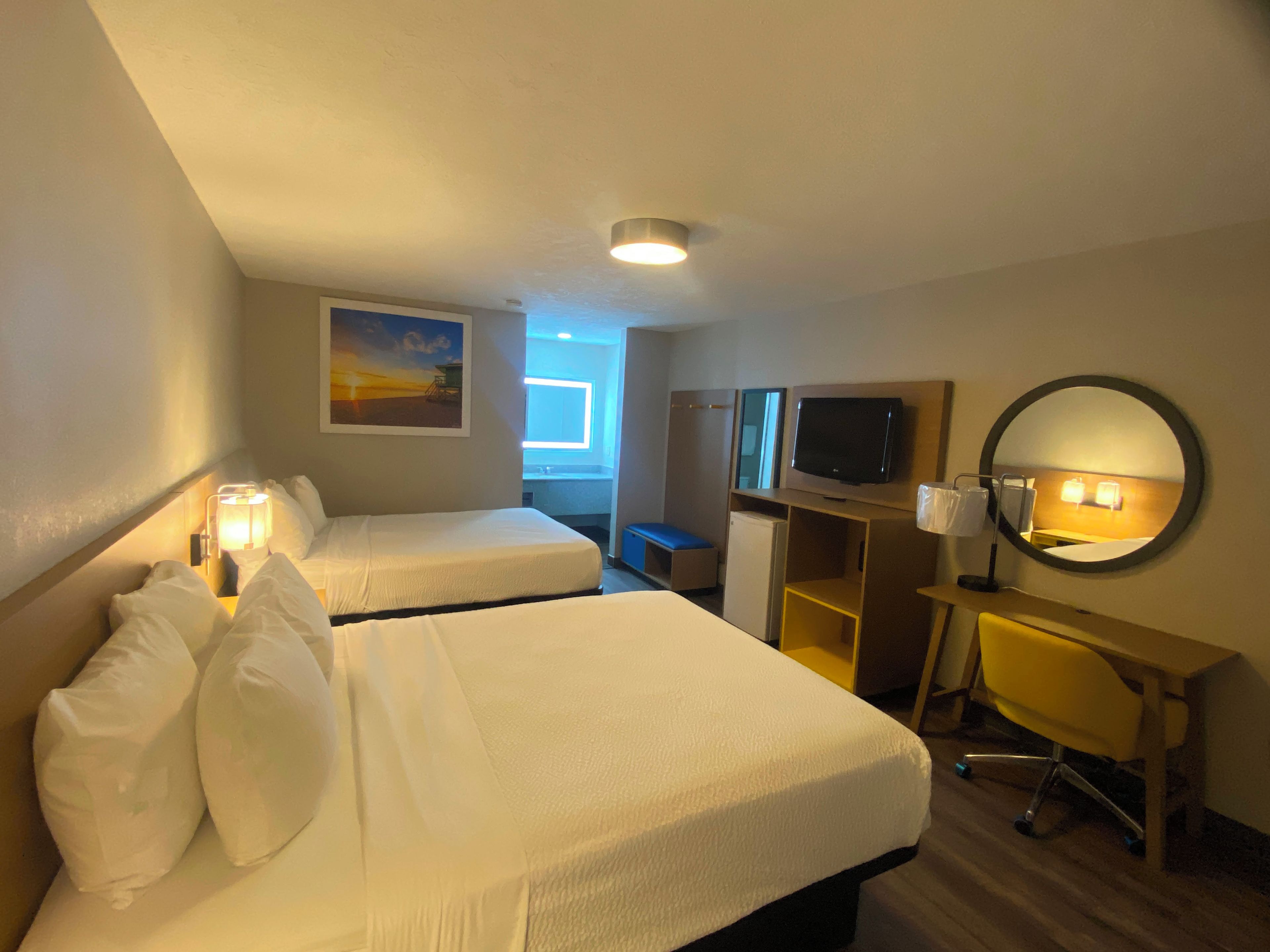 Ett hotellrum med två sängar, ett skrivbord, en tv, en spegel och ett fönster.