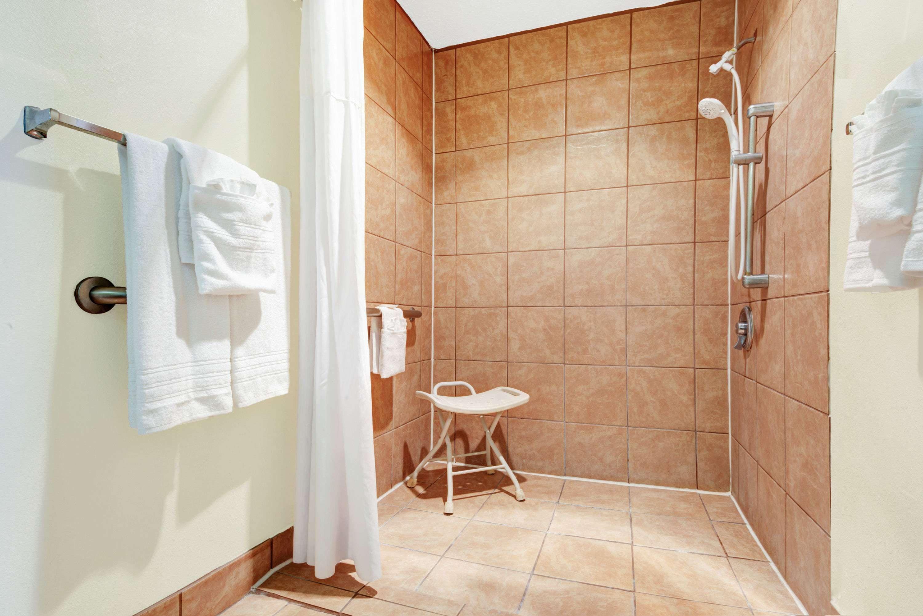 Un baño pequeño con azulejos, que incluye un cabezal de ducha blanco, un perchero blanco y un taburete plegable blanco.