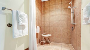 A small, tiled shower room with a white showerhead, a white towel rack, and a white folding stool.