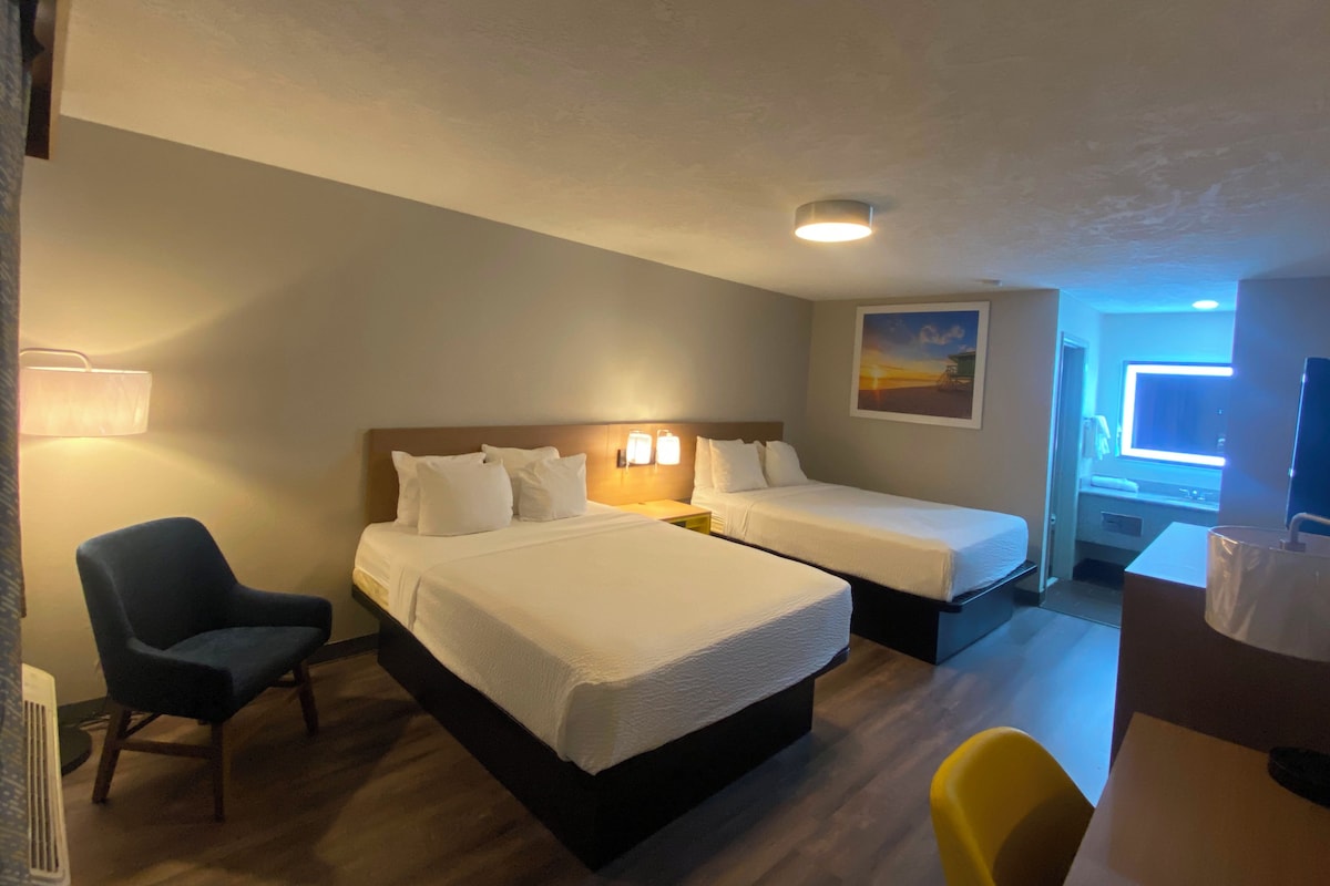 Habitación de hotel con dos camas, un escritorio, una silla y un cuadro en la pared.