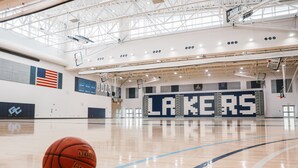 Una pista de bàsquet amb una pilota de bàsquet, un gran rètol que diu "LAKERS" i una bandera dels Estats Units a la paret.