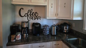 Cuina amb armaris blancs, senyal de barra de cafè i diverses cafetera i electrodomèstics.