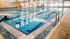 Una gran piscina coberta amb diverses pistes, un trampolí i una cadira de socorrista.