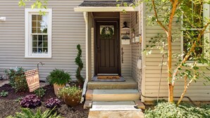A house with a dark front door, a welcome mat, and a small garden with various plants. - Walk to Uptown Westerville, Luxe Historic Charm (Westerville)