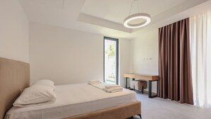 A modern bedroom with a large bed, a desk, and a view of the outdoors.