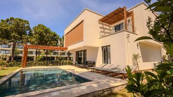 A modern two-story building with a swimming pool, outdoor seating, and a pergola.