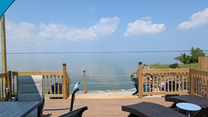 Una terraza de madera con sillones de descanso y una mesa, con vista a una masa de agua tranquila.