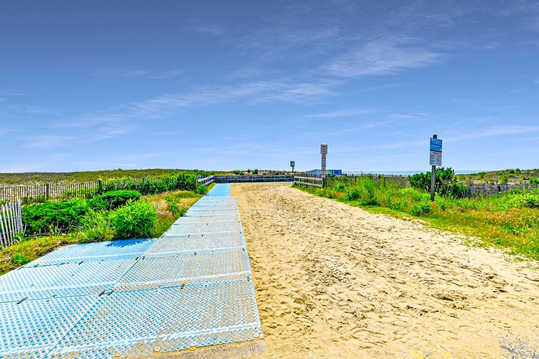 A beach pathway with a blue mat, sandy beach, and a fence.