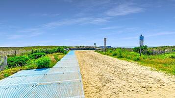A beach pathway with a blue mat, sandy beach, and a fence.