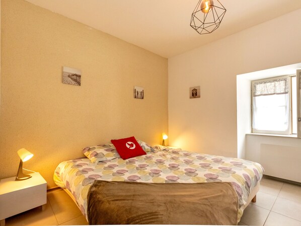 Quarto com uma cama, duas luminárias de cabeceira, uma luminária de teto geométrica e uma janela com cortina.