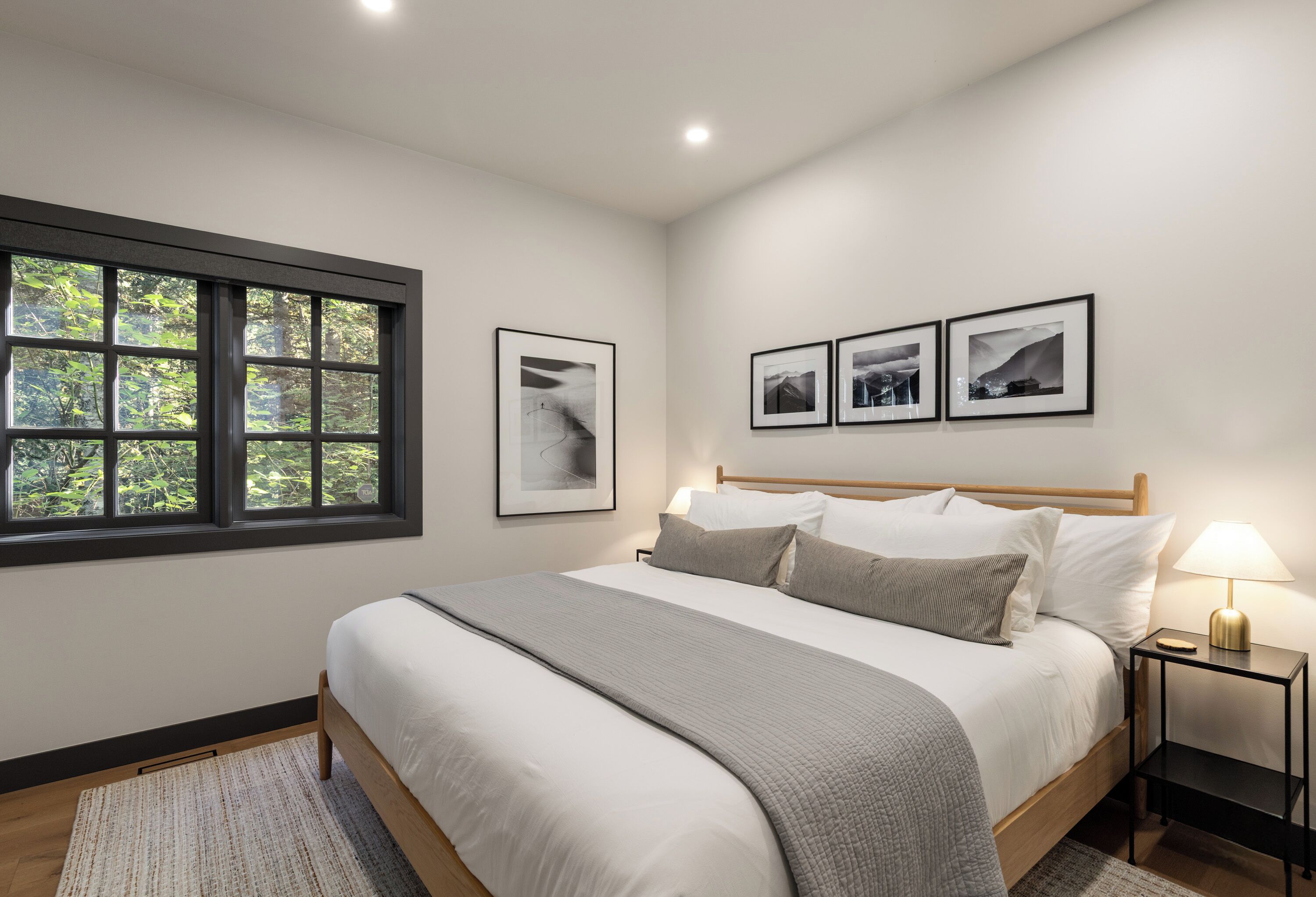 A bedroom with a large bed, a window with a view of trees, and three framed pictures on the wall.