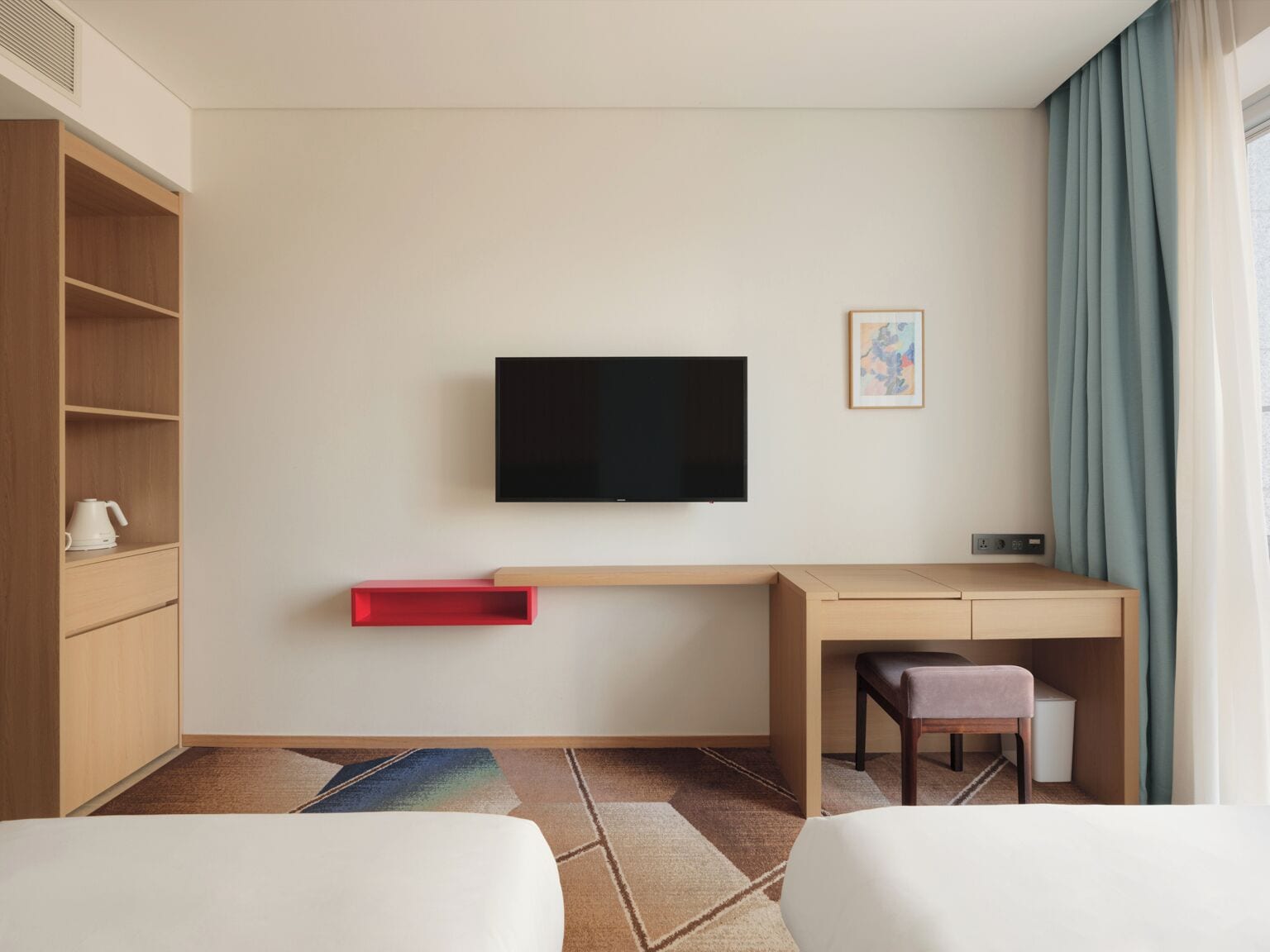 A hotel room with a bed, a desk with a chair, a TV mounted on the wall, and a small table with a chair.